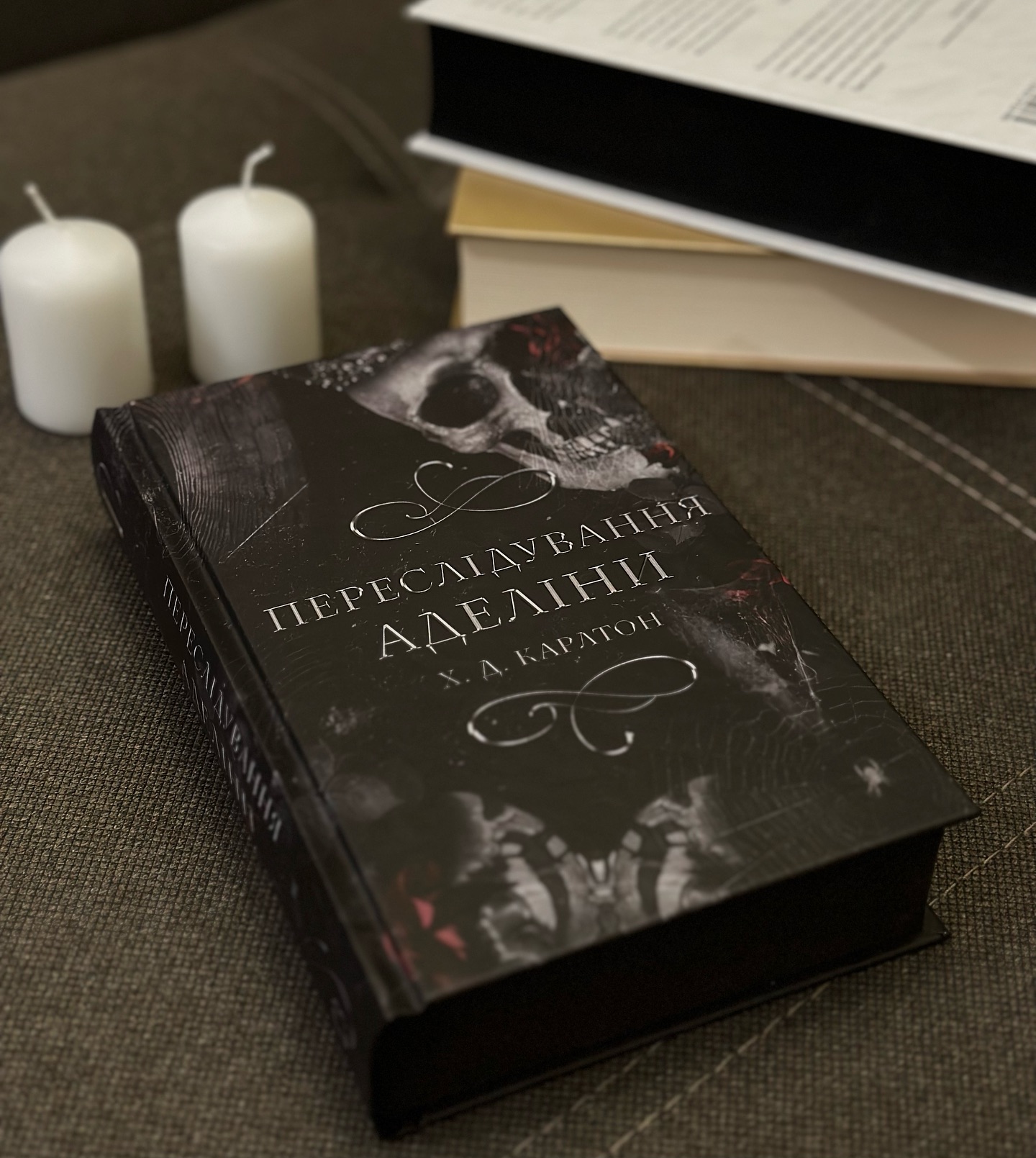 Чорна книга "Переслідування Аделіни" біля двої білих свічок